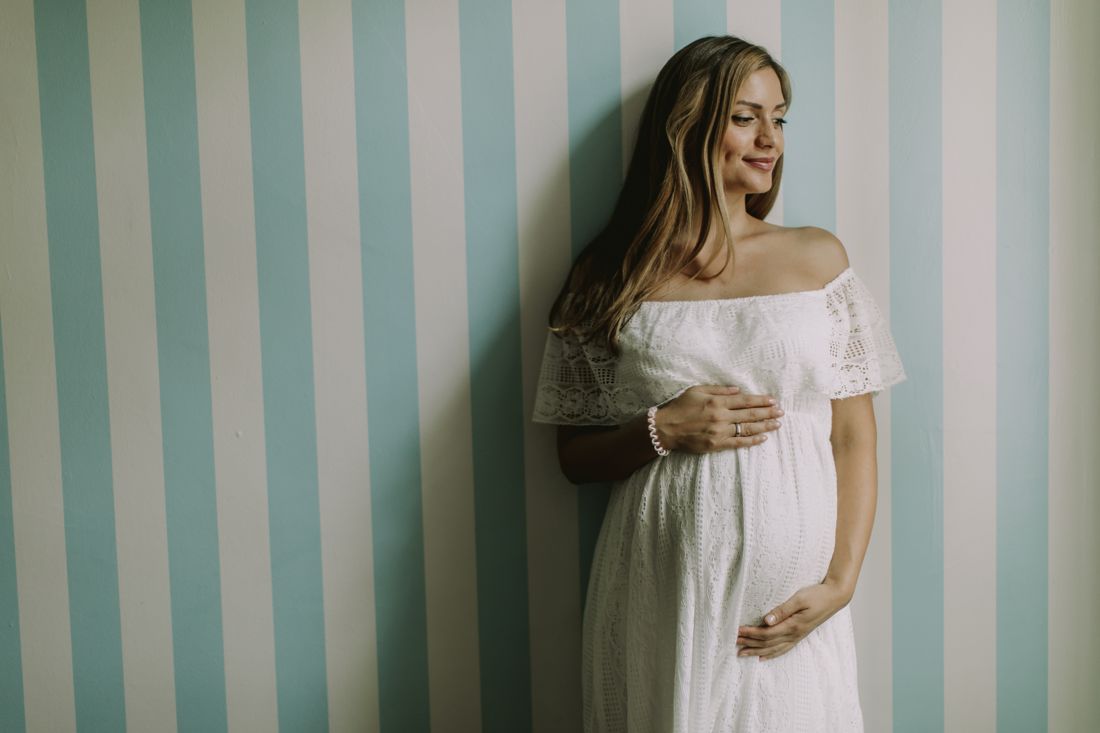 Mom-to-be in a white lace dress against a striped wall
