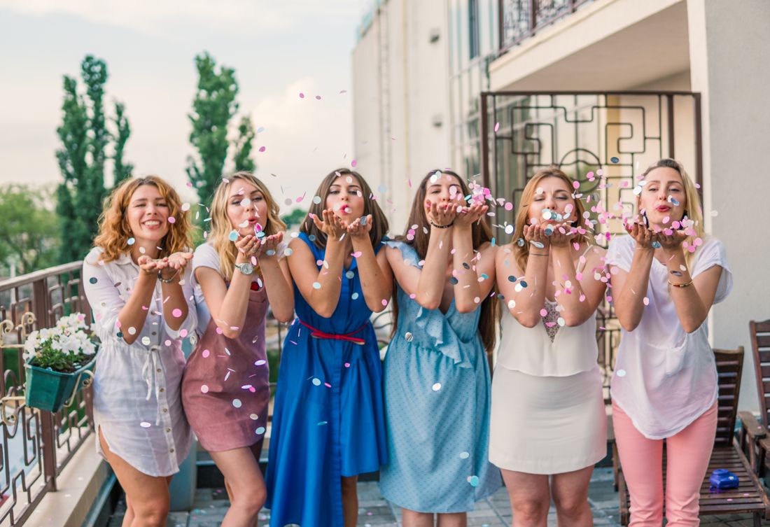 Women blowing confetti on a balcony in daylight