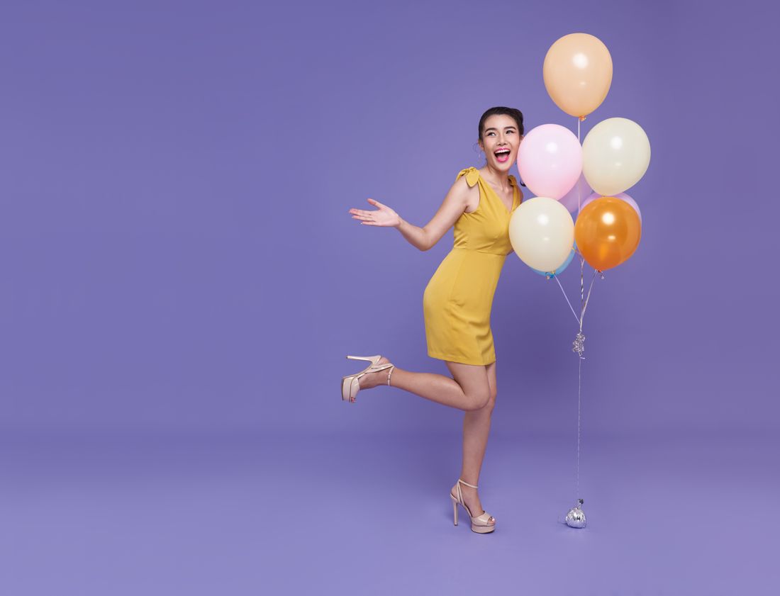 Model celebrating with balloons on a purple backdrop