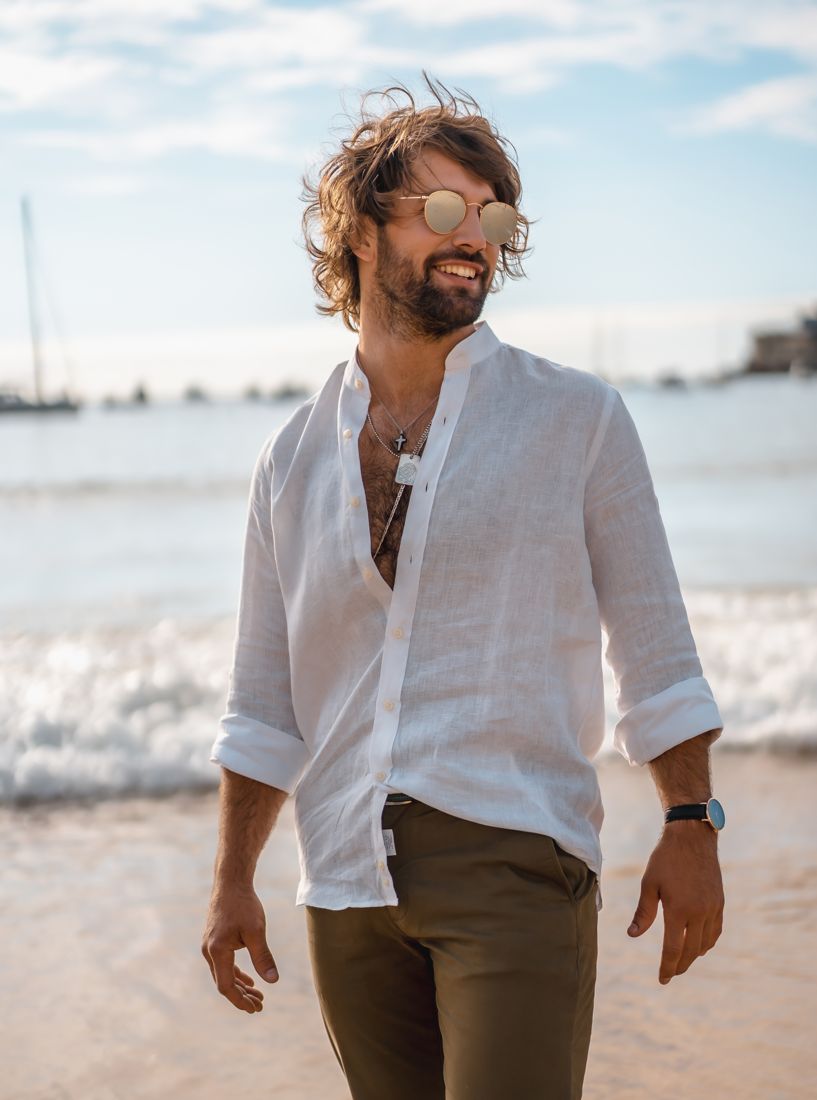 Man in an open white linen shirt walking the beach