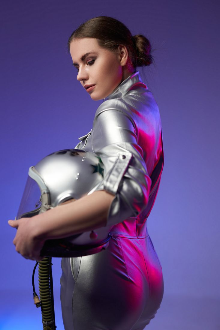 Silver-suited astronaut holding a helmet in pink and blue light