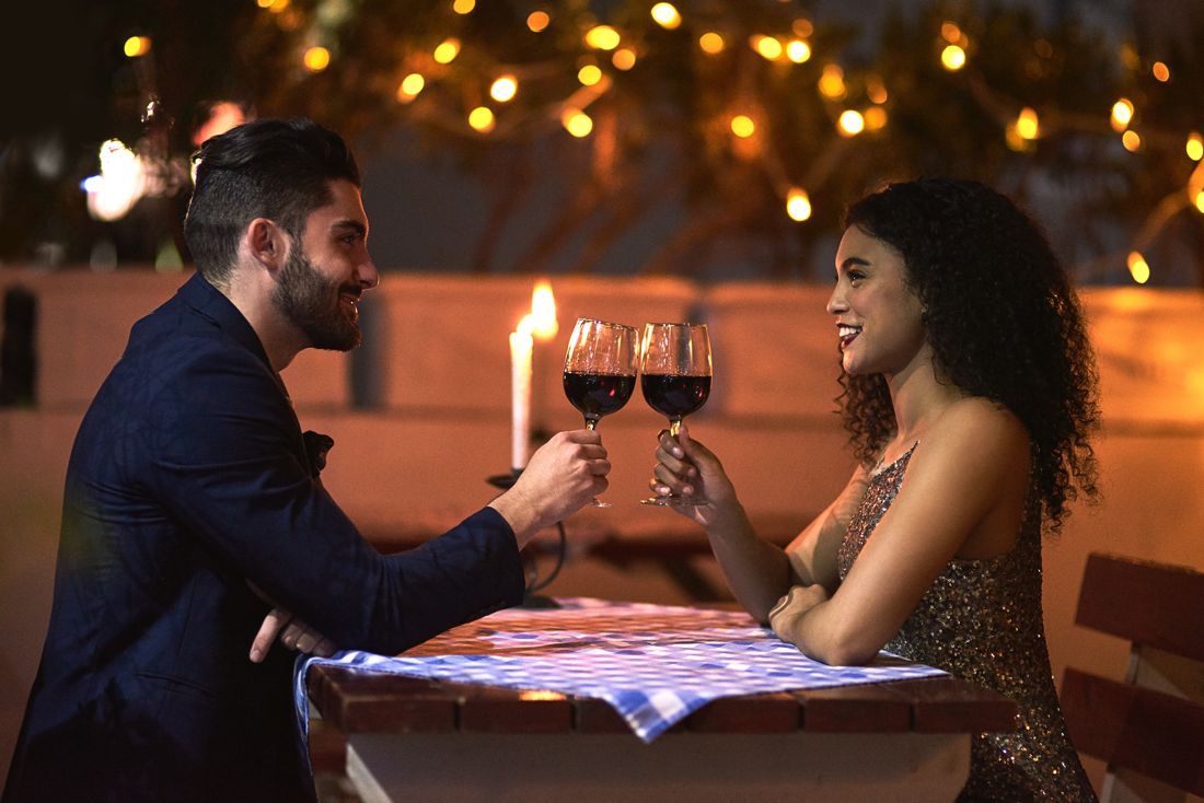 Couple toasting with red wine at a candlelit rooftop dinner