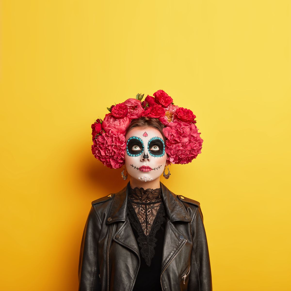 Striking Día de los Muertos makeup with red flower crown on yellow