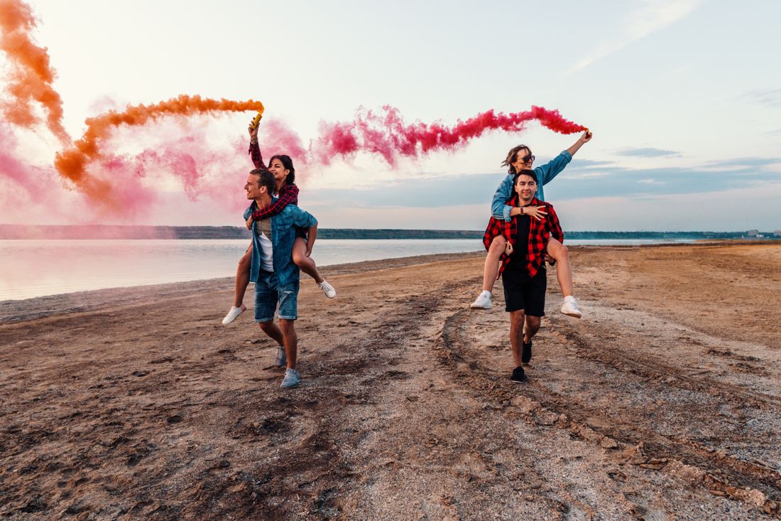 Couples with red and blue smoke bombs on a beach