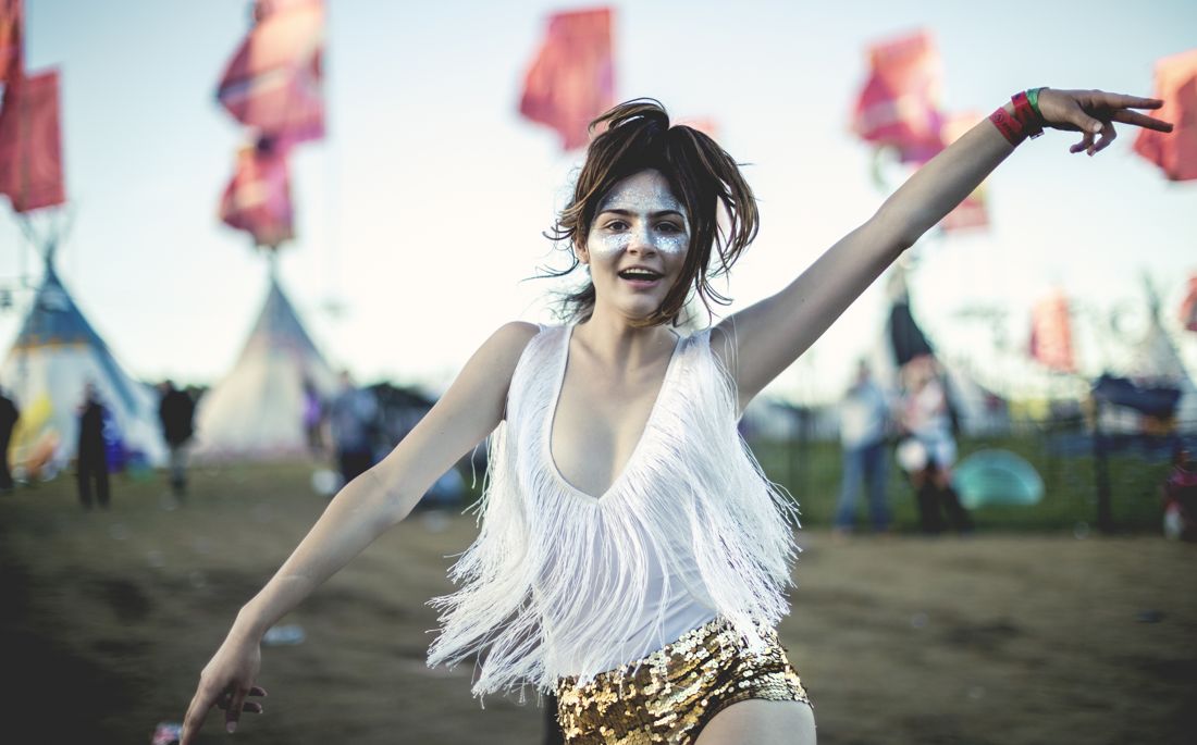 Fringe-top festival-goer dancing among tents and flags