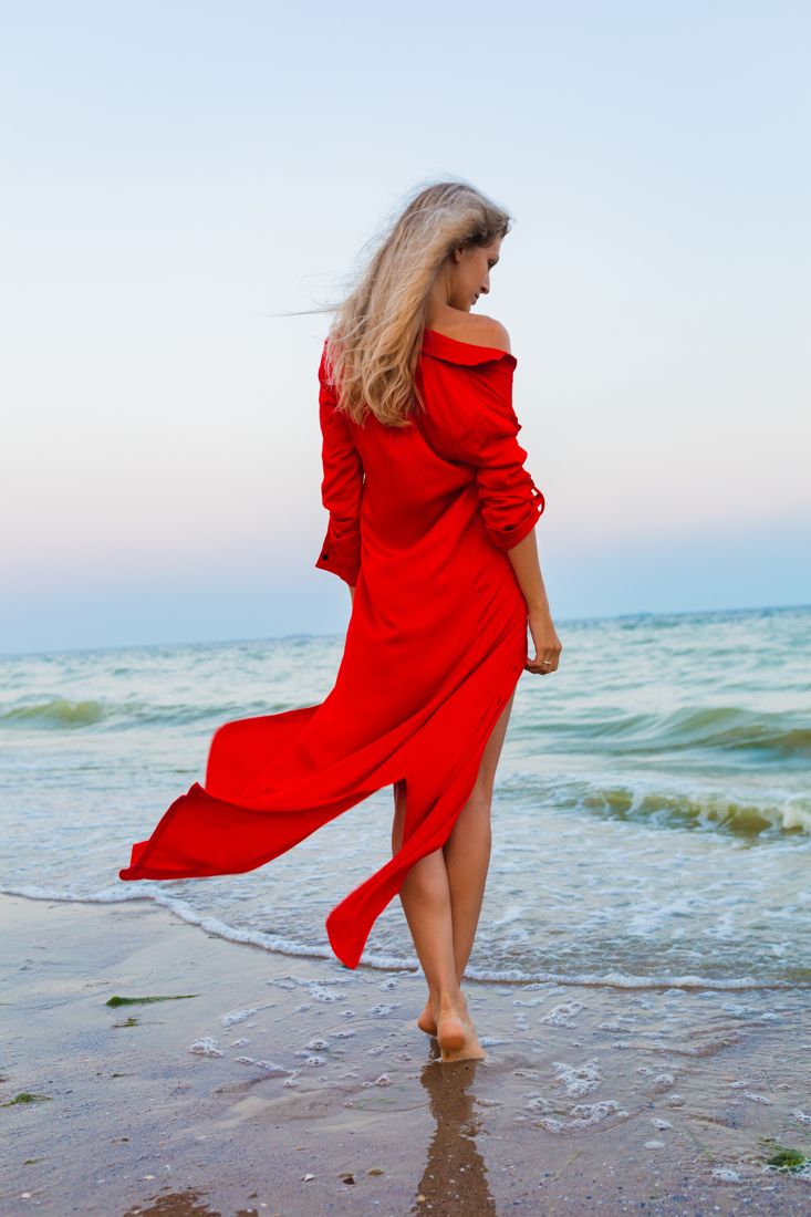 Red off-shoulder dress trailing in the surf