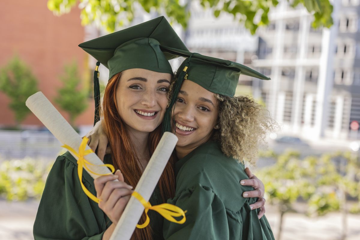 Two smiling graduates embracing holding diplomas