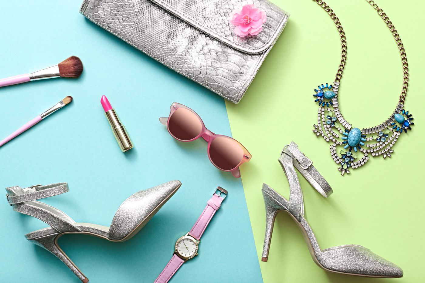 Flat lay of model accessories — heels, clutch, jewelry, sunglasses and makeup on a pastel background
