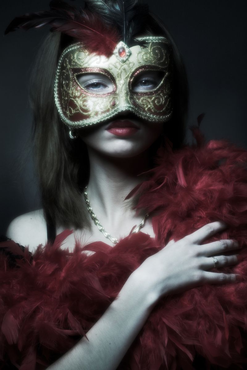 Model in a gold feathered mask against deep red