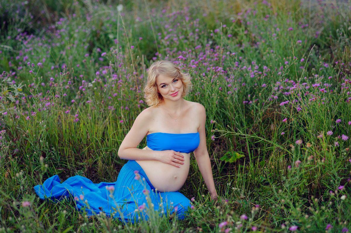 Expecting mother in a blue dress in a field of flowers