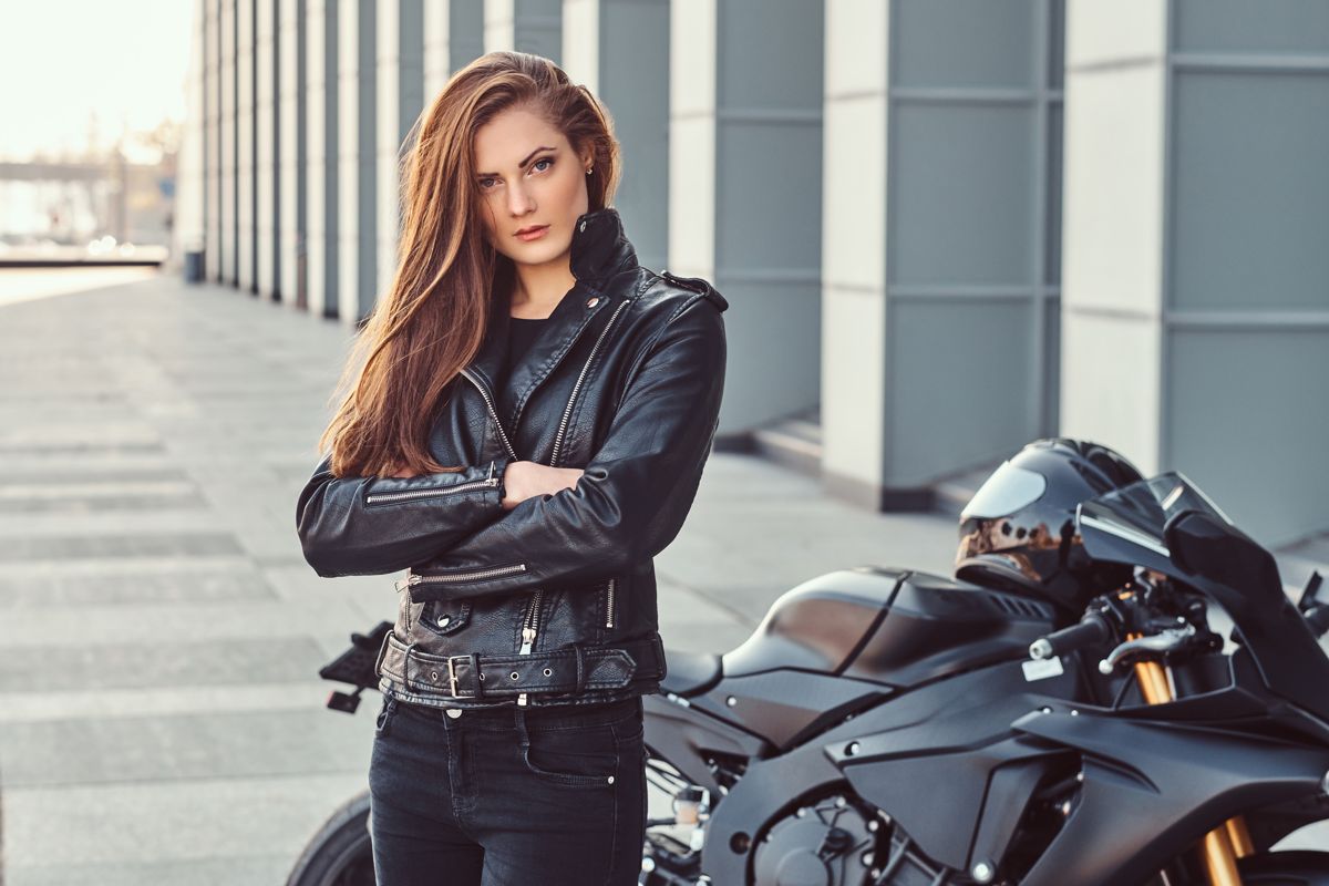 Biker in leather with arms crossed beside a motorcycle