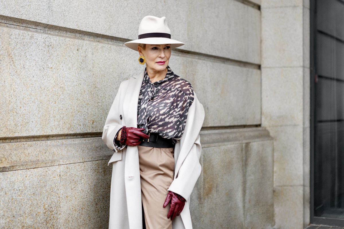 Silver-haired woman in a panama hat, white coat, leopard blouse and burgundy gloves