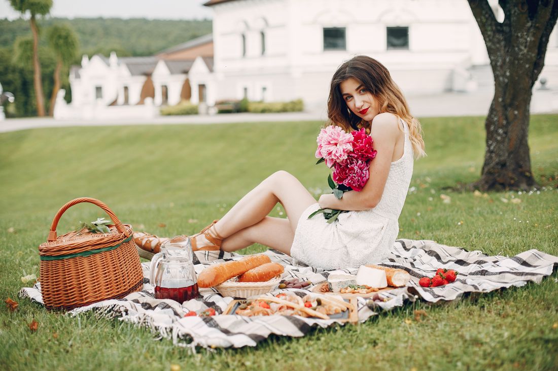 White dress and peonies on a picnic blanket on a manor lawn