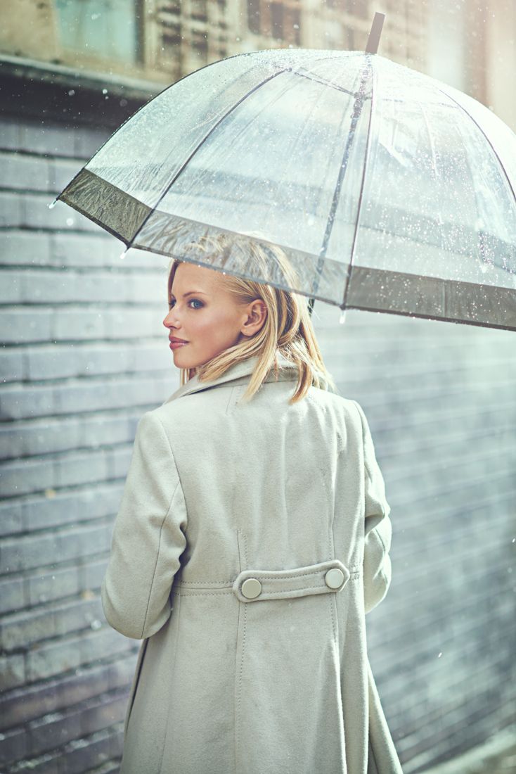 Blonde under a clear umbrella in a white coat