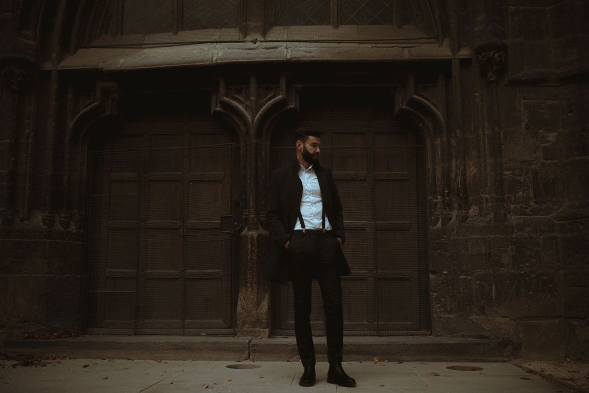 Bearded man in dark tailored suit before gothic architecture