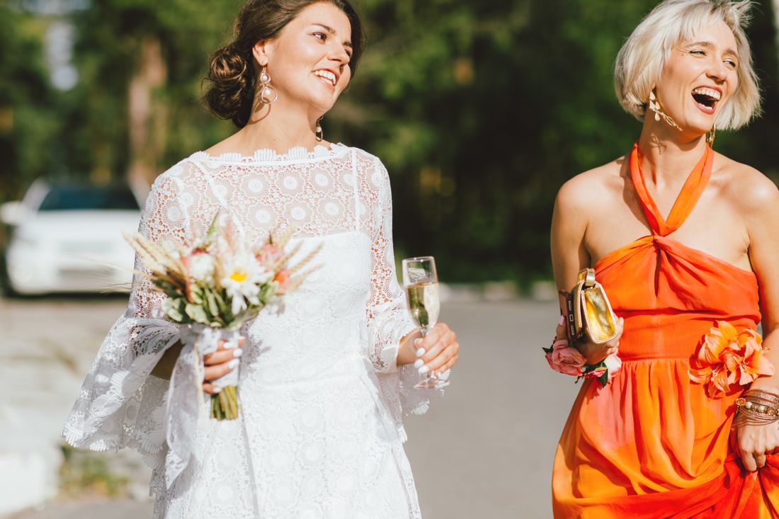 Bride and a wedding guest in an orange dress toasting in golden light