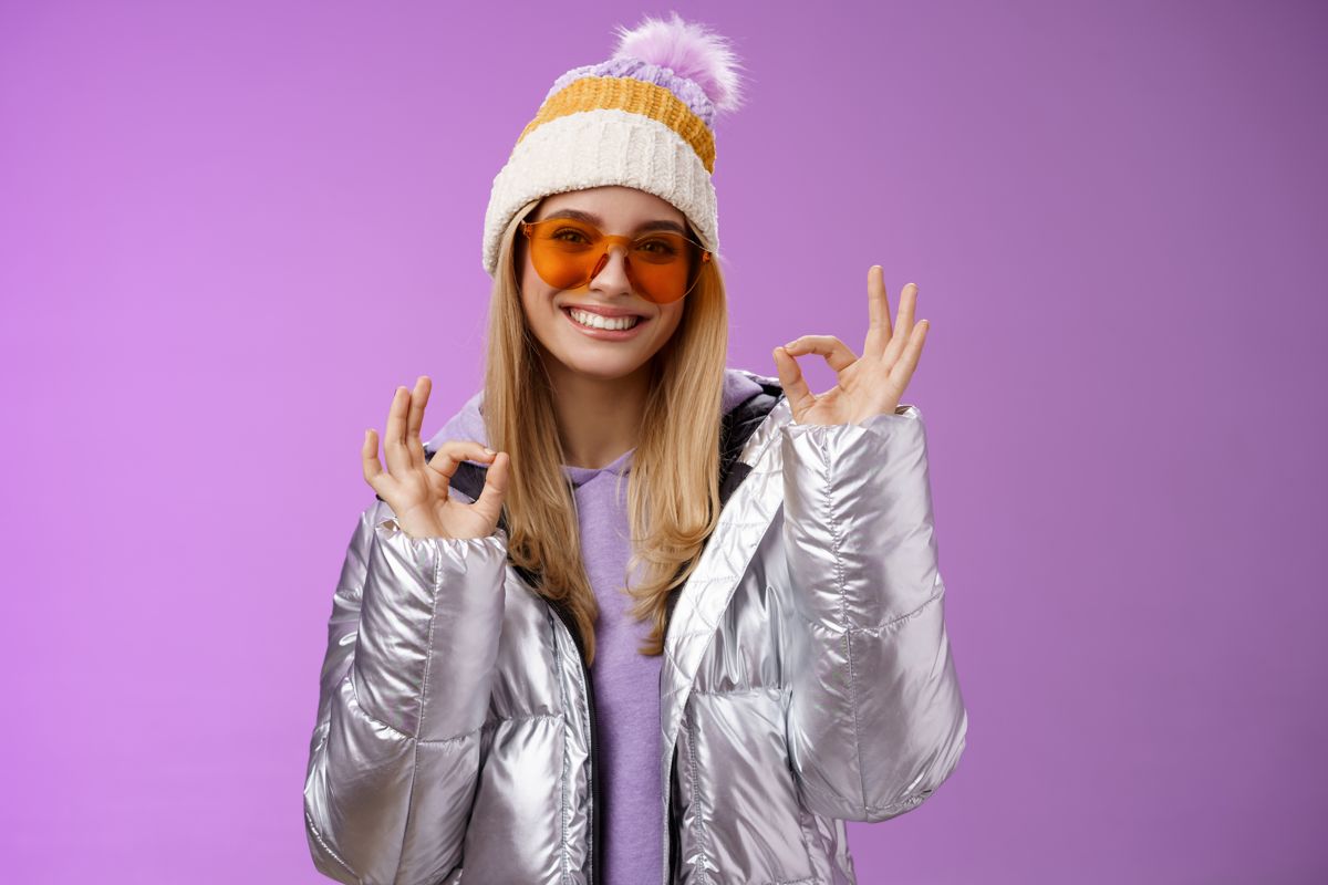 Model in a silver puffer and beanie against a lilac background