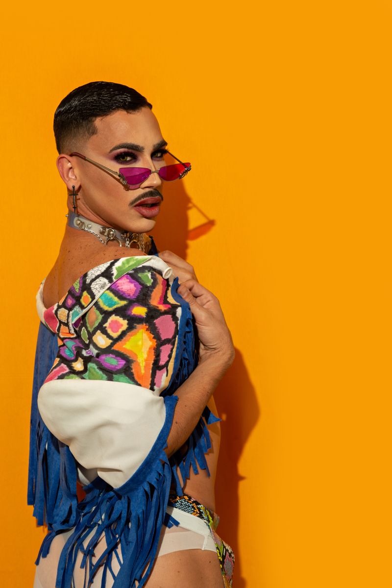 Model in colorful fringe and sunglasses on an orange backdrop